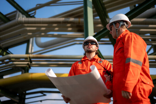 Engineers discussing project blueprint at industrial refinery site