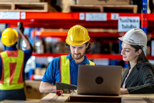 Collaborative logistics team reviewing stock availability in a large warehouse. Industrial specialist pointing at high shelves with a manager for inventory audit and strategic planning.