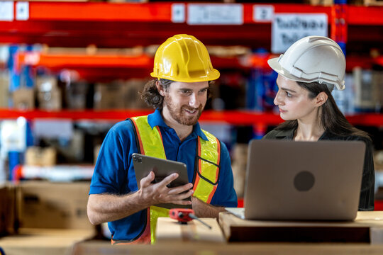 Collaborative logistics team reviewing stock availability in a large warehouse. Industrial specialist pointing at high shelves with a manager for inventory audit and strategic planning.