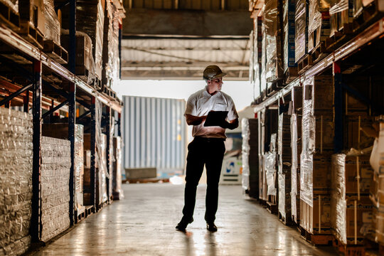 Silhouette of a supply chain coordinator inspecting high pallet racks and walking towards a shipping container dock inside a commercial logistics terminal.