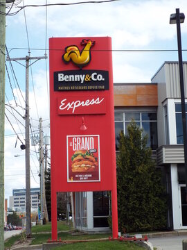 Gatineau, Quebec, Canada &ndash; May 2, 2026: A tall red "Benny & Co." Express restaurant pylon sign featuring a chicken logo stands outdoors on Boulevard Saint-Joseph.