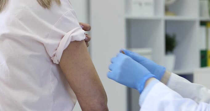 Doctor in medical gloves applying adhesive bandage onto patient's arm after vaccination in hospital, closeup