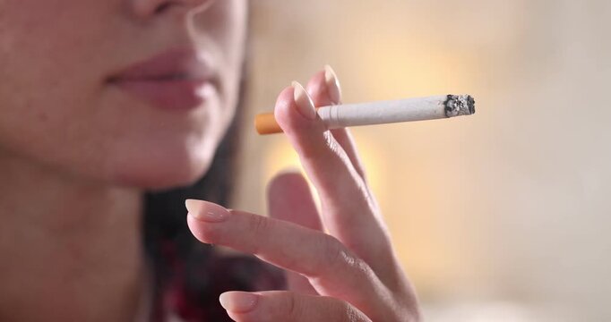 Woman smoking cigarette on blurred background, closeup
