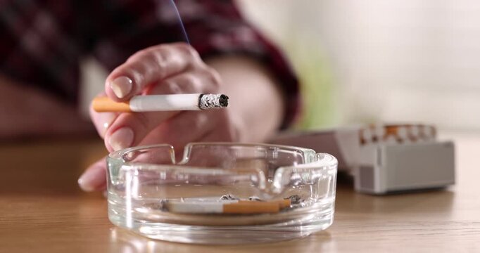 Woman with cigarette and ashtray at wooden table, closeup