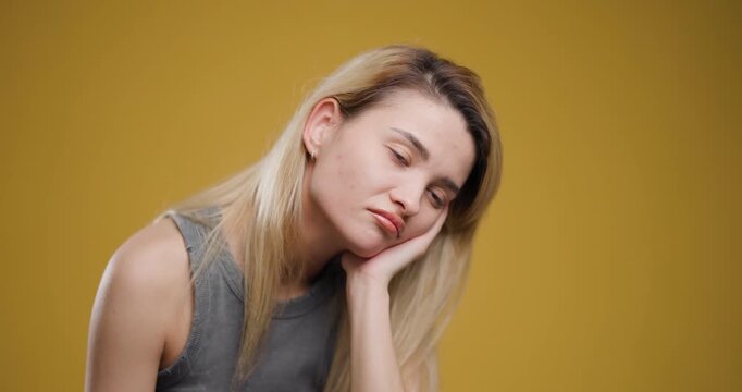 Portrait of a young blond woman expressing sadness against a yellow background