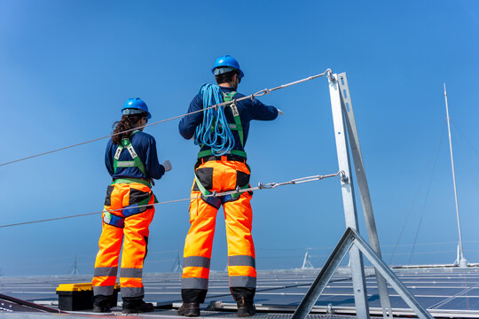 Technicians team working with safety equipment on industrial solar energy site, Workers wearing fall protection gear checking solar panel array efficiency