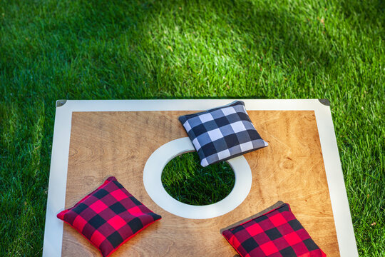 Overhead view of a corn hole board on grass with plaid bean bags on it