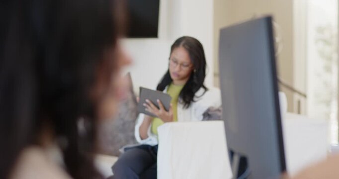 Diverse women reacting to focus, tucking hair, leaning to screen at home, background reading tablet