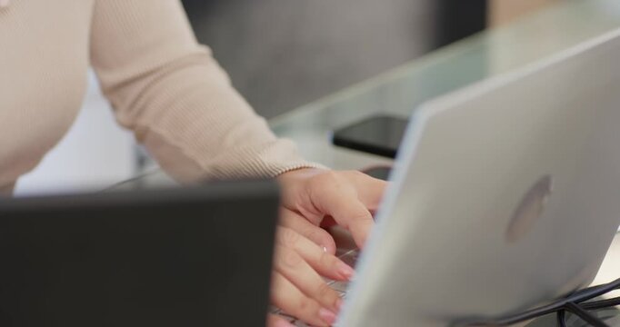 Woman in beige turtleneck typing and pausing while responding to email on silver laptop at desk
