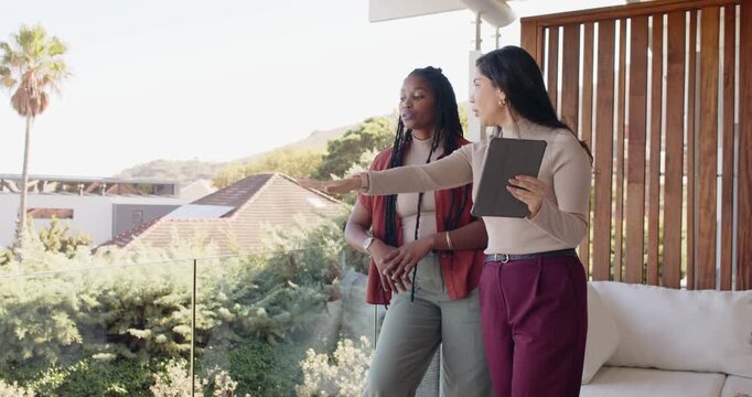 Diverse women agent briefing client on balcony, tablet leading agent pointing at roofs, copy space