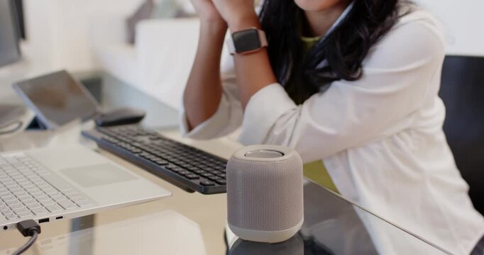 Adult African American woman speaking to voice speaker, camera shifting, typing email at glass desk
