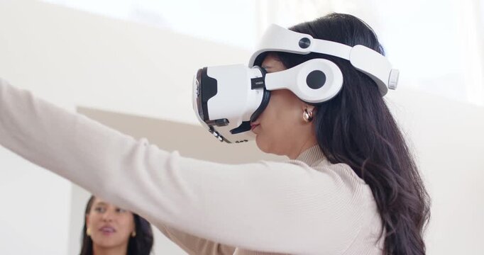 Female duo in demo room, VR user heeding app prompts, extending hands as observer checking tablet