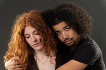 Obraz premium Mixed race couple standing close, man embracing woman with head on shoulder, representing diversity and love