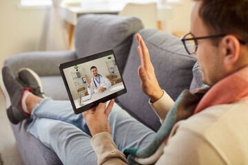 Cropped shot of sick young man using digital tablet, having online consultation with doctor. Unhealthy patient waving hand during video call, using remote telemedicine services to ask for advice.