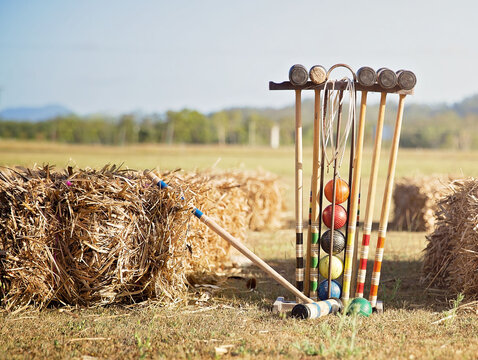 Colorful croquet equipment arranged beside hay bales on a sunny rural field, capturing a relaxed outdoor lawn game atmosphere with vintage sporting charm.