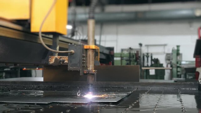 Industrial CNC plasma cutting machine processing metal sheet with sparks in factory. Automated metal fabrication and manufacturing technology.