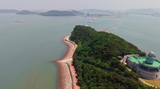 Aerial flyover along coastline of Nue Island above  Lighthouse Observatory uncovering giant wind turbines of Tando Sea Road in shallow sea water