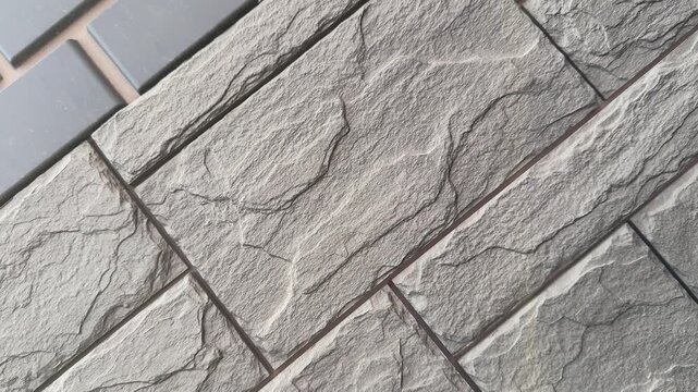Close-up grey stone facade panel showing textured masonry and grout lines, staggered rectangular modules with visible seams
