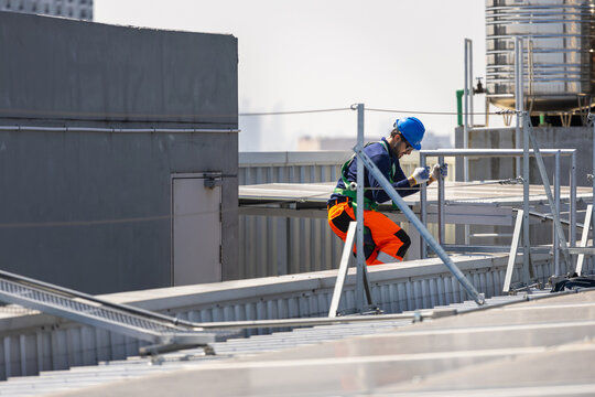 Technician working with safety harness on commercial rooftop solar site, Worker performing maintenance on rooftop infrastructure with fall protection, Man climbed down the ladder on construction site