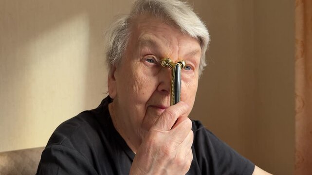Elderly woman facial massage golden massager close-up, seated grandmother uses dual roller gold massager along jawline and cheek