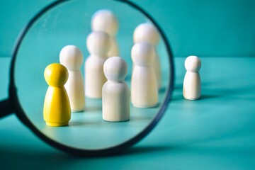 Obraz premium Magnifying Glass Focusing on Yellow Wooden Figure in Group