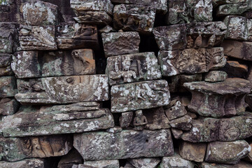 Fototapeta premium Ancient stone carvings of figures and mythical creatures adorn the weathered walls of Bayon Temple, Angkor Wat, Siem Reap, Cambodia, showcasing intricate Khmer artistry.