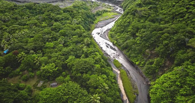 Aerial drone footage capturing the winding river through lush tropical rainforest and volcanic landscape near Port Resolution village on Tanna Island, Vanuatu, showing vibrant green vegetation