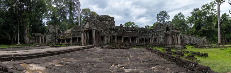Fototapeta premium The ancient ruins of Preah Khan temple in Siem Reap, Cambodia, overgrown with trees, showcase the enduring power of nature reclaiming historical architecture.