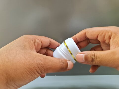Sidoarjo, Indonesia - 24 May, 2026: Hand holding an unbranded open white cosmetic jar of skin brightening gel cream on a neutral grey background