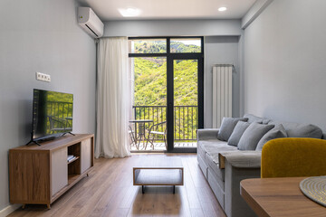 Fototapeta premium Modern living room with large window and balcony overlooking green hills, cozy apartment interior