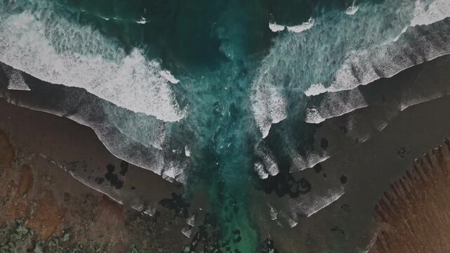 Crashing white foamy waves meeting sandy and rocky Melasti Beach shoreline in Bali, Indonesia, captured from aerial perspective, highlighting the power and natural beauty of the ocean. Aerial top down