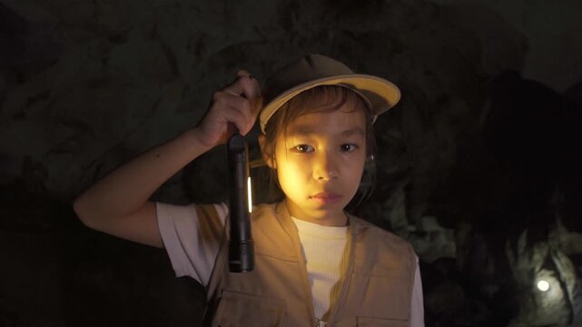 Little Asian girl explorer holding up a flashlight to illuminate a dark underground cave.