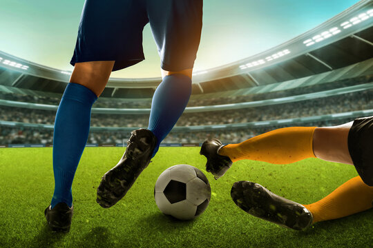 Two professional soccer player legs, blue sock dribbling ball and yellow sock sliding tackle in the stadium field
