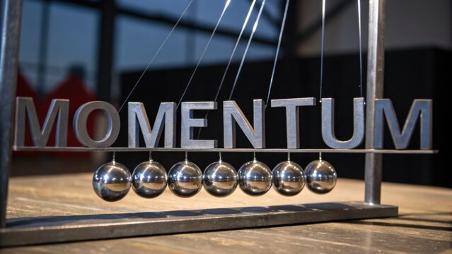 Kinetic energy demonstration with pendulum balls displaying momentum principle in modern workspace on wooden table with sunlight streaming in