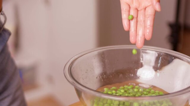 Person washing fresh green peas in a glass bowl