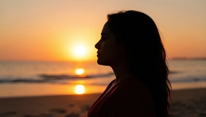Fototapeta premium Serene Sunset Reflection: A solitary woman stands silhouetted against a breathtaking sunset on a tranquil beach, her profile serene as the golden sun dips below the horizon.