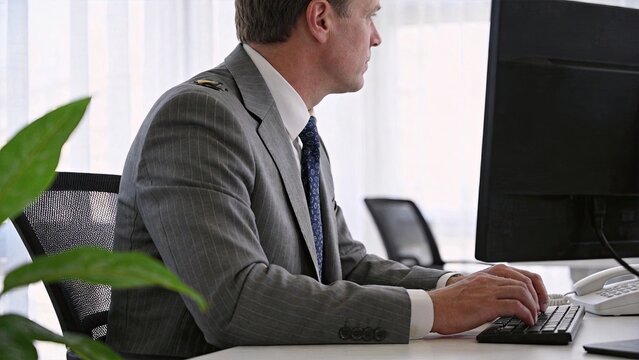 Professional businessman in grey suit working on desktop computer, focused male employee typing keyboard in modern bright office, corporate technology concept, side view portrait