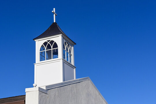 Church steeple with a bell, cross, and arched windows against a clear blue sky, representing religious architecture, faith communities, and spiritual landmarks