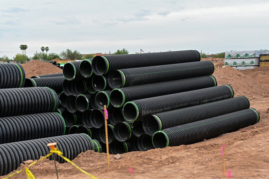 Stacked corrugated drainage pipes stored at a residential development site, representing underground utility infrastructure, stormwater systems, and residential construction materials