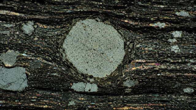Intense microscopic texture observed within petrographic thin section revealing hydraulic fracturing embedment in dark shale geology, showing complex pattern