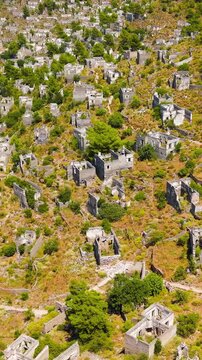 Vertical video. Kayakoy, Turkey. Hundreds of abandoned stone houses and crumbling ruins cascading down arid mountain slopes, aerial drone view under bright summer sunlight and clear sky. Aerial View.