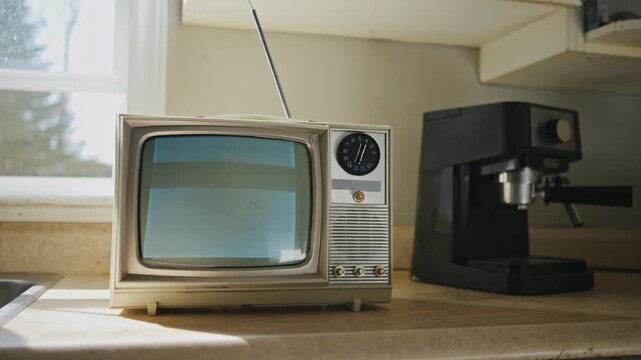 camera pan across a vintage kitchen reveals a small black-and-white television displaying analog no-signal static interference. Evocative cinematic footage with a melancholic, timeless quality. 