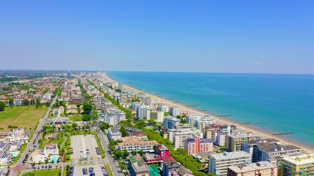 Italy, Jesolo. Aerial panoramic sweep over Lido di Jesolo, the long sandy beach and dense resort skyline stretching along the turquoise Adriatic Sea under clear summer sky. Drone footage