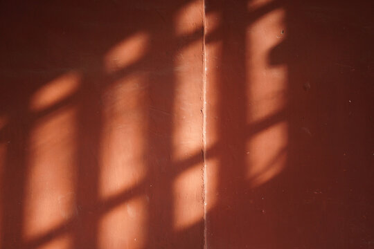 Shadow of bars cast on a reddish wall creating an interesting pattern
