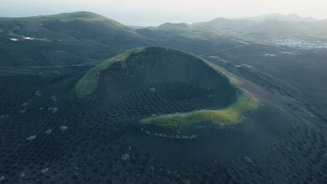 La Geria, Lanzarote, Spain, aerial drone shot of a crater-like volcanic vineyard formation, revealing the surrounding volcanic landscape and vineyards