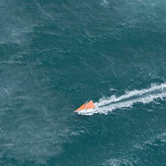 Obraz premium Deep teal sea water surface with a small coral sailboat creating a white wake for travel advertising, marine sport promotion and coastal lifestyle background
