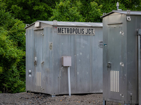 Metal railroad signal bungalows and utility equipment sheds labeled Metropolis Jct standing by a gravel trackbed