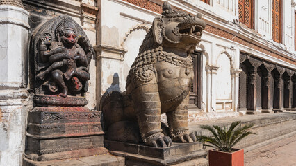 Obraz premium Stone statue of a lion on a pedestal. Mouth open, big teeth. On the wall of the building is a bas-relief of a god Hanuman, eviscerating the demon Hiranyakashipu. Nepal. Kathmandu. Durbar Square.