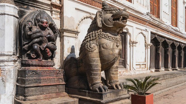 Stone statue of a lion on a pedestal. Mouth open, big teeth. On the wall of the building is a bas-relief of a god Hanuman, eviscerating the demon Hiranyakashipu. Nepal. Kathmandu. Durbar Square.