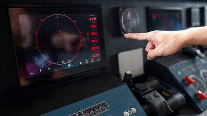 Captain hand pointing at marine radar monitor screen or GPS navigation map on boat dashboard. Nautical vessel control system in wheelhouse or ship bridge. Modern boating technology and operation © zephyr_p